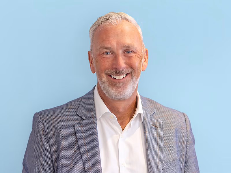 Professional portrait of man in grey blazer and white shirt against blue background